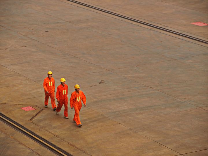 Drie medewerkers in oranje werkkleding en helm op een werfterrein